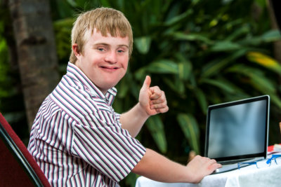 Portrait of handicapped student doing thumbs up sign next to laptop outdoors.