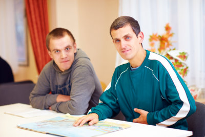 Cheerful adult men with disability sitting at the desk in rehabilitation center and read books
